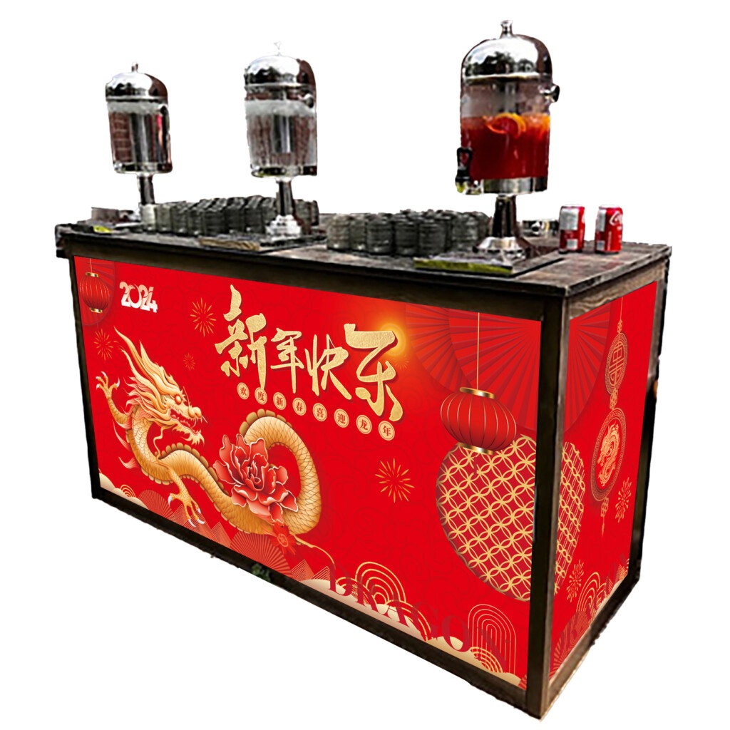 A vibrant Lunar New Year themed serving bar, decorated with a bold red and gold dragon design, symbolizing prosperity and good fortune. The front panel displays intricate patterns, Chinese characters, and traditional lantern illustrations. On the bar top, there are two large drink dispensers filled with beverages, alongside neatly stacked rows of clear cups. To the side, a small stack of red beverage cans are visible, adding to the festive color scheme